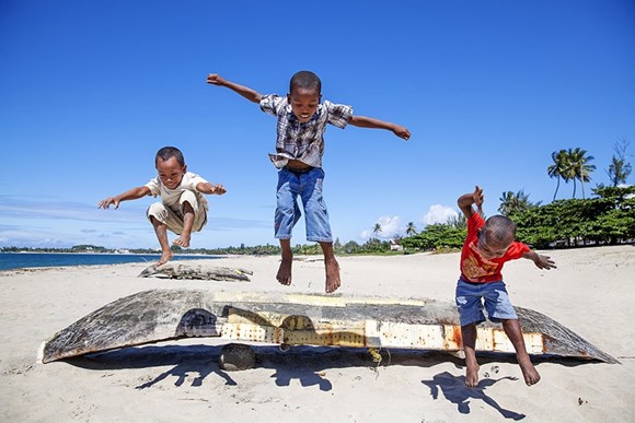 tres niños saltan sobre un barco en la orilla del mar